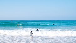 夏の大浜海岸で、子供たちが楽しそうに泳ぐ様子。透き通った青い海に白い波が立ち、夏のレジャーを満喫しています。
