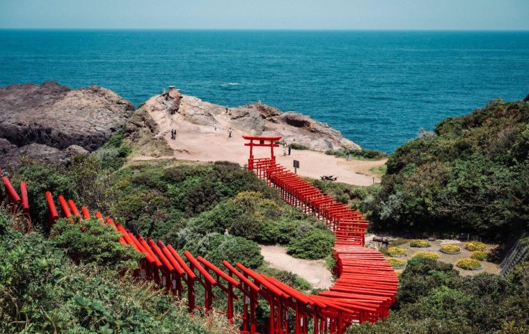 日本海の青い海と緑の崖に沿って、朱色の鳥居が連なる元乃隅神社の全景。