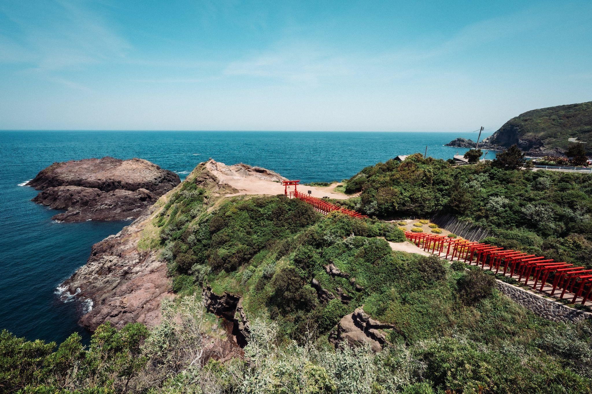 広大な日本海と緑の丘陵に囲まれた、元乃隅神社の鳥居が連なる壮大な景色。